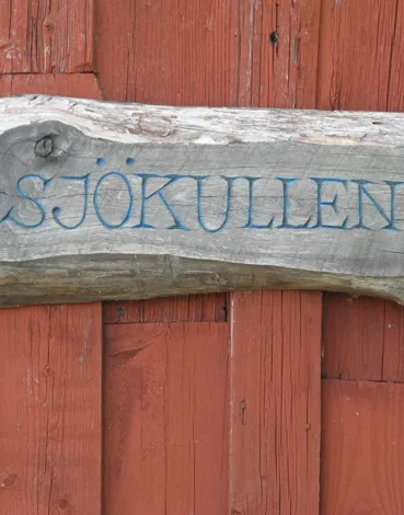 Handmålad träskylt med texten Sjökullen på en röd vägg